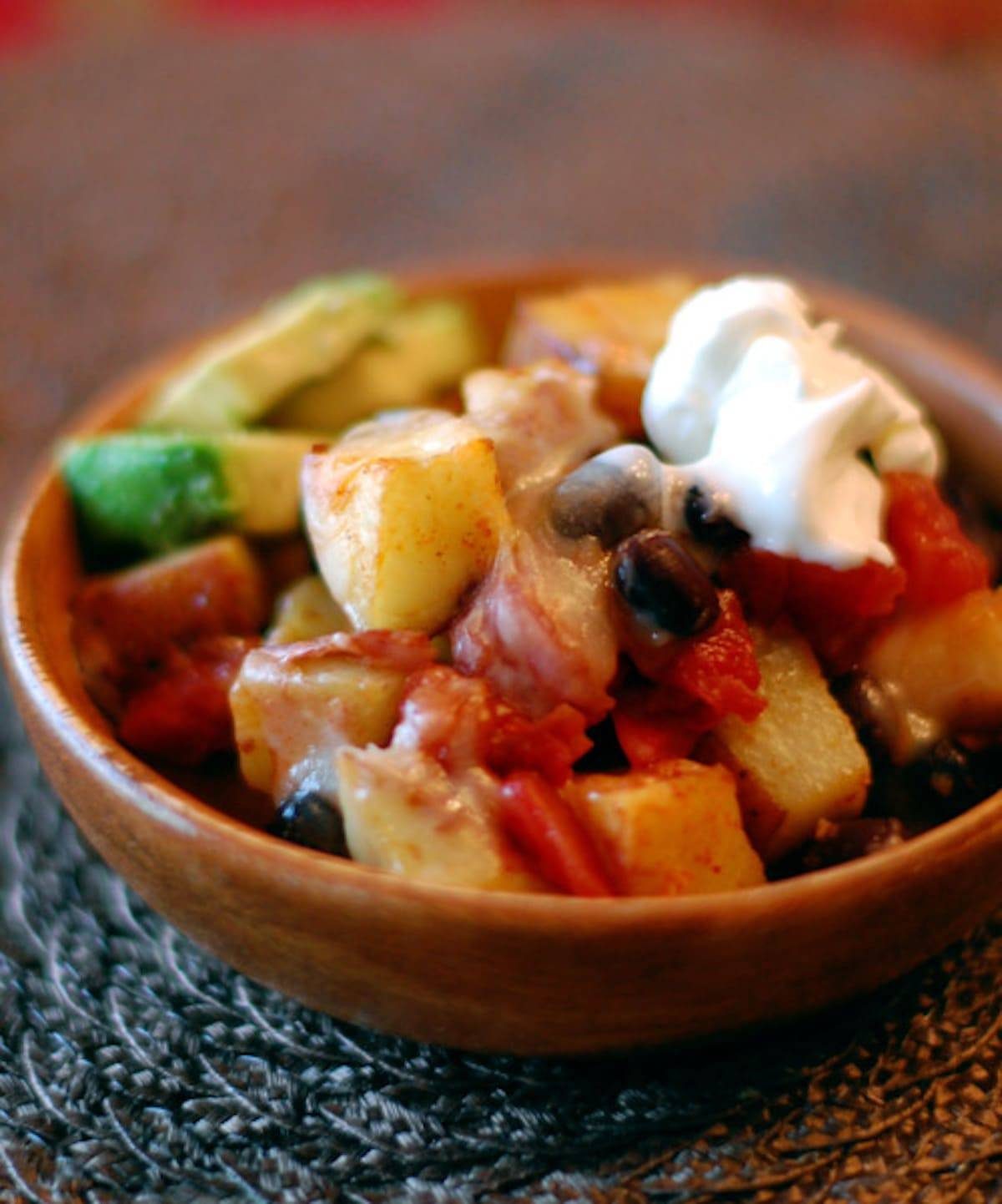 Cheesy roasted potato nachos in a wooden bowl with sour cream topping.