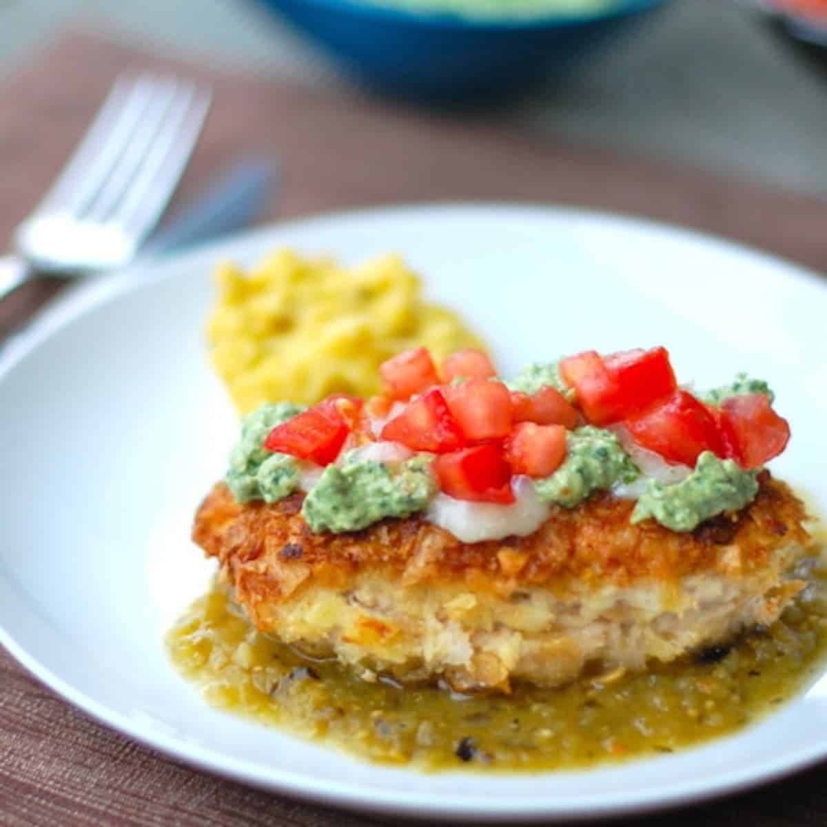 Tortilla chicken with salsa verde is chicken coated with corn tortilla chips and topped with salsa verde on a white plate.