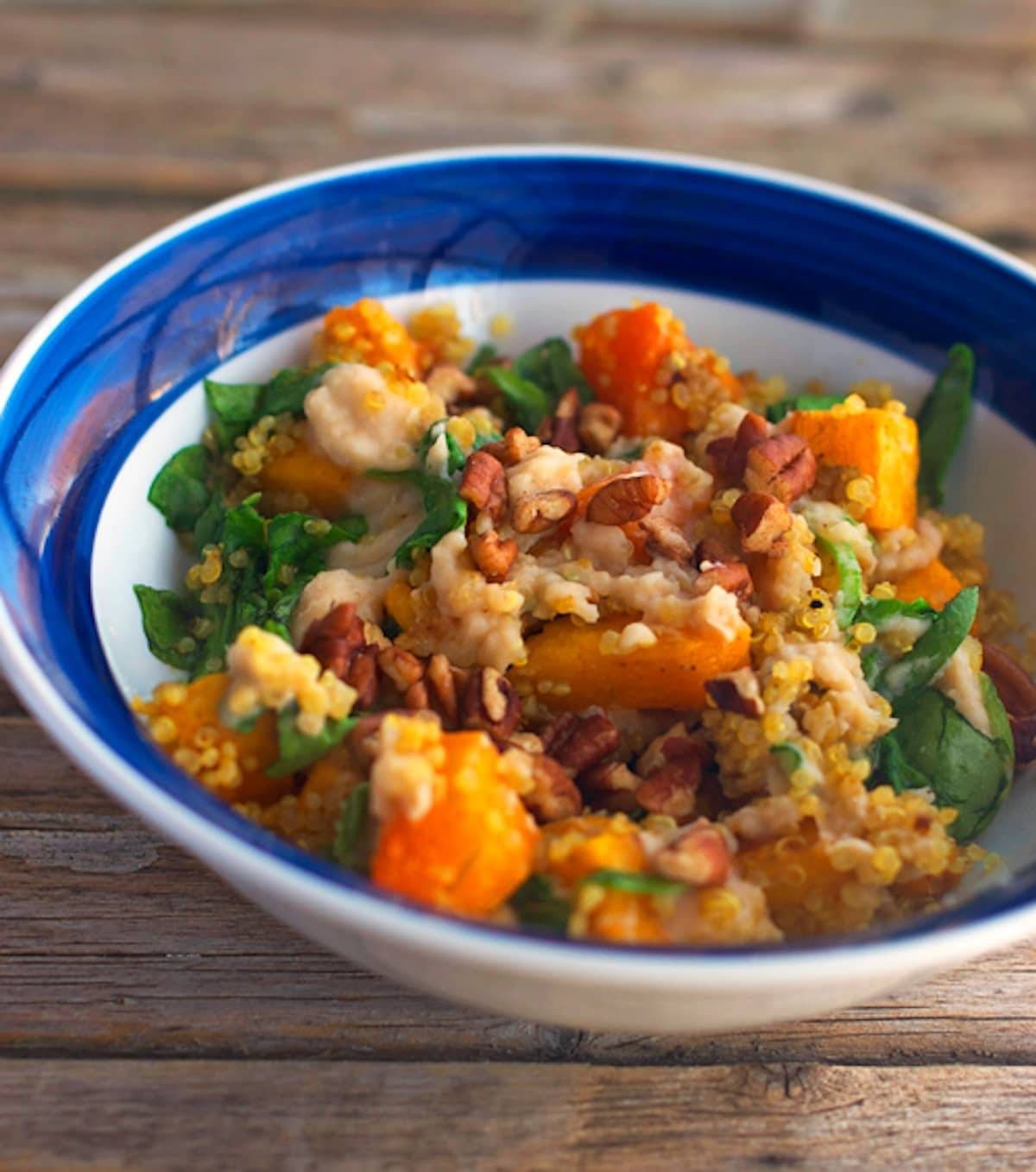 Sweet quinoa squash bowl that includes fresh spinach, hummus, butternut squash, pecans, and quinoa.