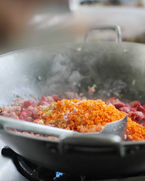 Adding veggies to the wok with sausage and hot dogs.