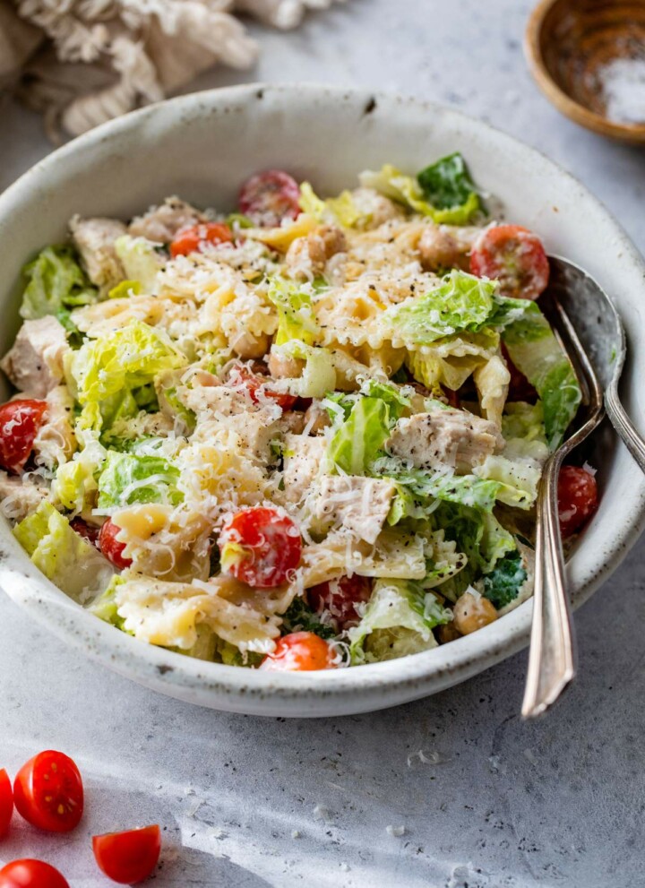 Chicken caesar pasta salad served in a small white bowl with a fork and spoon.