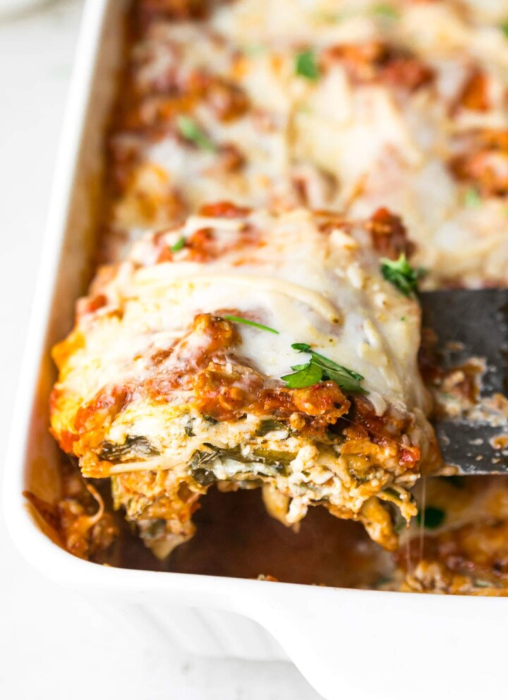 Serving a slice of turkey spinach lasagna out of a casserole dish.